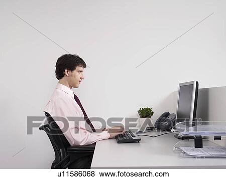 Stock Photo - Male office worker using computer at desk in office. Fotosearch