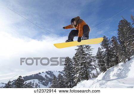 Male snowboarder jumping over snow covered hill, mid air View Large Photo Image Picture - Male snowboarder jumping over snow covered hill, mid air. Fotosearch