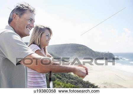 Stock Photo - Man and Daughter Looking out at Ocean from balcony of vacation house, side view. Fotosearch