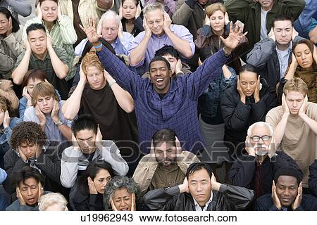 Stock Image - Man celebrating among crowd covering ears. Fotosearch