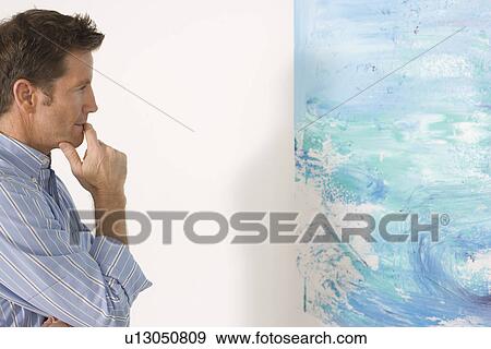 Stock Photo - Man contemplating paintings in gallery. Fotosearch