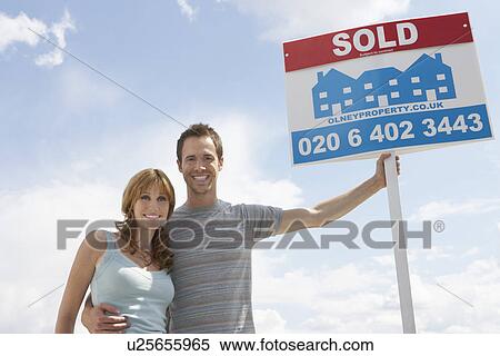 Man embracing woman, holding sold sign against sky View Large Photo Image Stock Photography - Man embracing woman, holding sold sign against sky. Fotosearch