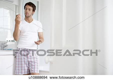 Picture - Man in bathroom reading label of pill bottle. Fotosearch