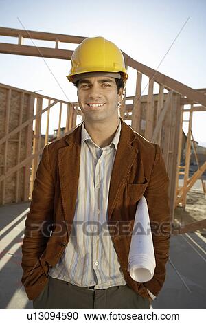 Stock Image - Man in hard hat on building site with blue prints. Fotosearch