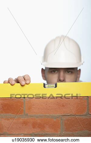 Man in hard hat using level to check brick wall, high section View Large Photo Image Stock Image - Man in hard hat using level to check brick wall, high section. Fotosearch
