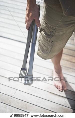Man in shorts Holding Tongs on wooden porch, low section, high angle view View Large Photo Image Stock Photo - Man in shorts Holding Tongs on wooden porch, low section, high angle view. Fotosearch