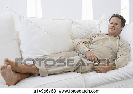 Man listening to MP3 player on sofa in living room, portrait View Large Photo Image Stock Image - Man listening to MP3 player on sofa in living room, portrait. Fotosearch