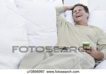 Stock Photo - Man listening to MP3 player on sofa in living room. Fotosearch