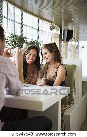 Man Photographing smiling Friends sitting side by side in cafe View Large Photo Image Stock Image - Man Photographing smiling Friends sitting side by side in cafe. Fotosearch