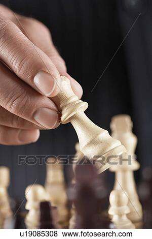 Stock Photo - Man playing chess, close-up of hand holding piece. Fotosearch