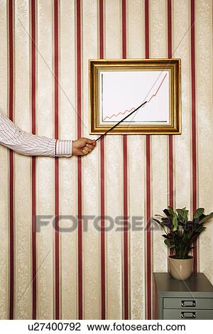 Stock Image - Man pointing to framed graph on office wall, close-up of arm and hand. Fotosearch
