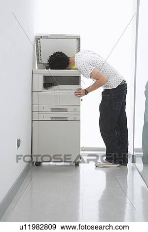 Stock Photo - Man putting his head in copy machine in hallway. Fotosearch