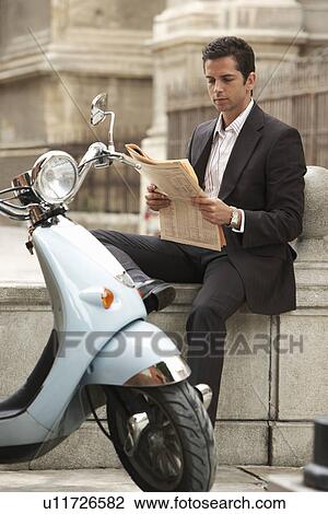 Stock Image - Man sitting by scooter, reading newspaper.. Fotosearch