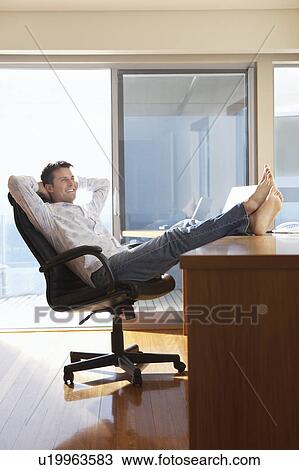 Stock Image - Man sitting in office with feet up on desk.. Fotosearch