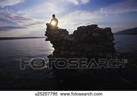 Stock Photography - Man sitting on rock overlooking ocean. Fotosearch
