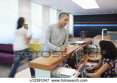 Stock Photo - Man standing at reception desk, Talking to Receptionist. Fotosearch