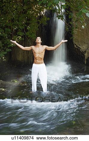 Man standing in river by waterfall meditating, front view, full length View Large Photo Image Picture - Man standing in river by waterfall meditating, front view, full length. Fotosearch