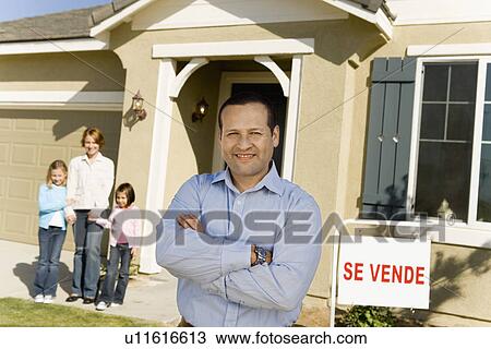 Stock Image - Man standing near family in front of house for sale. Fotosearch