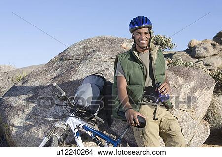 Man stands leaning against rock with mountain bike View Large Photo Image Picture - Man stands leaning against rock with mountain bike. Fotosearch