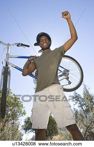 Man stands with arm raised holding a mountain bike View Large Photo Image Stock Photo - Man stands with arm raised holding a mountain bike. Fotosearch