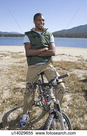 Stock Photography - Man stands with mountain bike and arms folded. Fotosearch