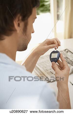 Stock Photo - Man Using Blood Sugar Meter in living room. Fotosearch