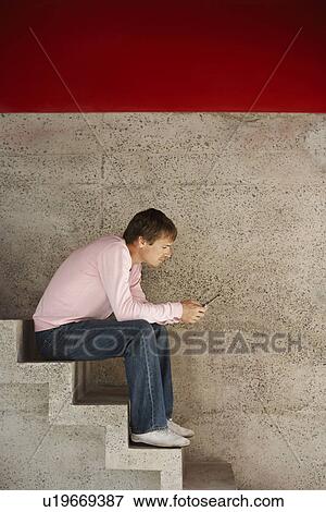 Stock Photo - Man using cell phone sitting on stairs, side view. Fotosearch