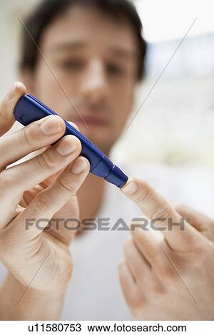 Stock Image - Man using lancelet on finger in bathroom, close up. Fotosearch