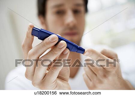 Stock Photograph - Man using lancelet on finger in bathroom, close up. Fotosearch