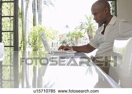 Man using laptop on dining table, side view View Large Photo Image Stock Photography - Man using laptop on dining table, side view. Fotosearch