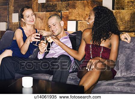 Man with two women toasting, sitting on couch in bar View Large Photo Image Stock Photography - Man with two women toasting, sitting on couch in bar. Fotosearch