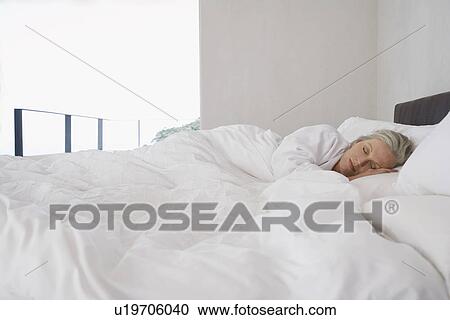 Stock Image - Mature woman lying asleep in bed. Fotosearch