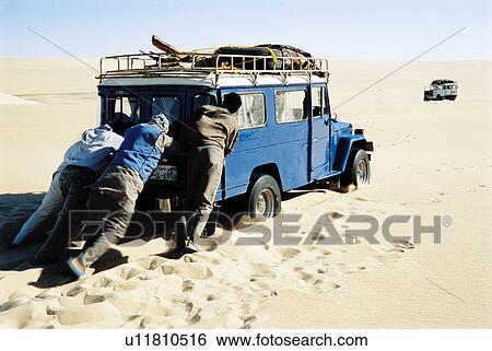 Stock Photograph - Men pushing jeep in desert. Fotosearch