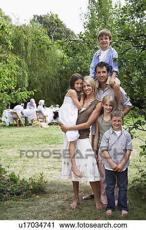 Stock Image - Mid-adult couple and four kids (7-10) in garden, other family members in background. Fotosearch