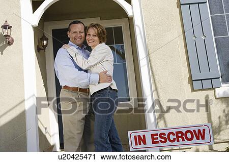 Stock Image - Mid-adult couple in front of new house, portrait. Fotosearch