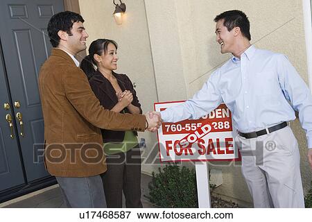 Stock Photo - Mid adult couple in front of their new home. Fotosearch