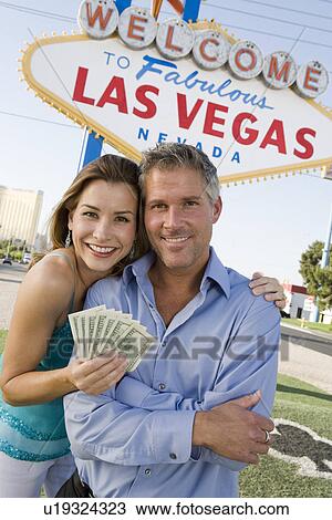 Stock Image - Mid-adult couple in front of Welcome to Las Vegas sign, portrait. Fotosearch