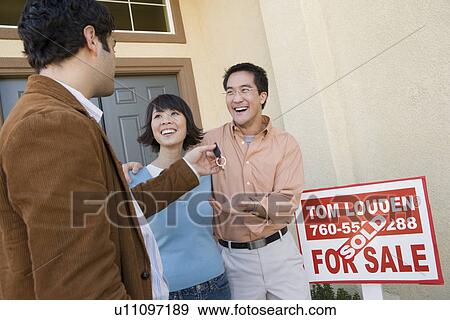Stock Photo - Mid adult couple receiving keys to their new home. Fotosearch