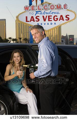 Stock Photo - Mid-adult couple sitting in limousine and drinking champagne in front of Welcome to Las Vegas sign. Fotosearch
