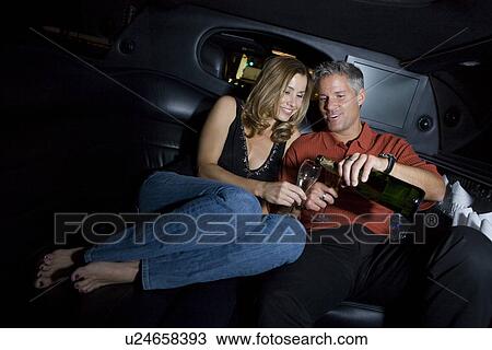 Stock Image - Mid-adult couple sitting on back seat of limousine and drinking champagne. Fotosearch