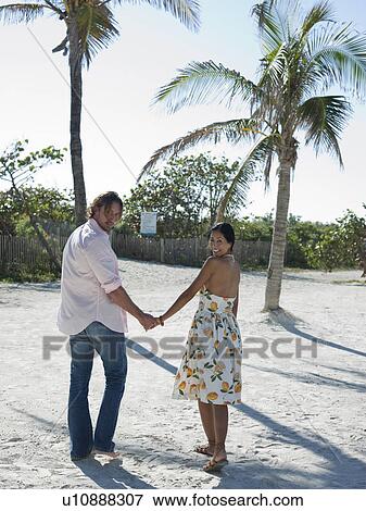 Stock Photo - Mid-adult couple walking on beach. Fotosearch