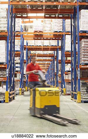 Stock Image - Mid-adult Man Driving Pallet Jack Through Warehouse. Fotosearch