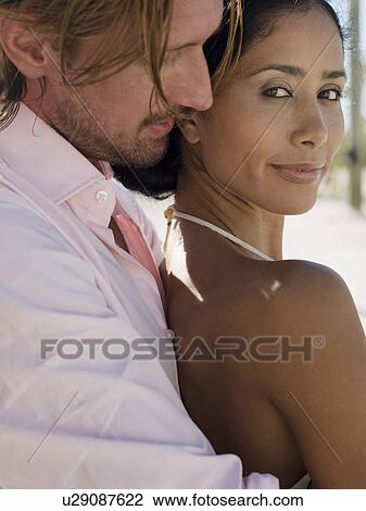 Stock Image - Mid-adult man embracing mid-adult woman, head and shoulders. Fotosearch