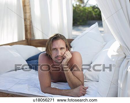 Stock Image - Mid-adult man lying down on bed outside. Fotosearch