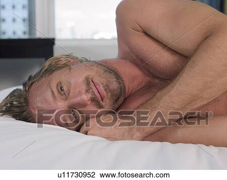 Stock Image - Mid-adult man lying on bed, head and shoulders. Fotosearch