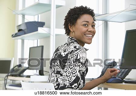 Mid-adult office worker sitting by desk View Large Photo Image Stock Image - Mid-adult office worker sitting by desk. Fotosearch