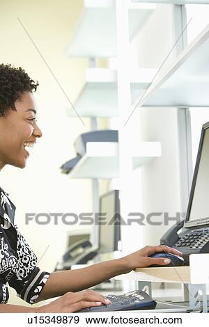 Stock Photo - Mid-adult office worker sitting by desk. Fotosearch