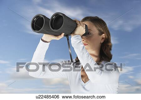 Stock Photograph - Mid-adult woman standing outside, looking through large pair of binoculars. Fotosearch