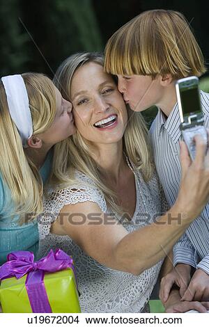 Mid-adult woman taking photograph with mobile phone of her with two children View Large Photo Image Picture - Mid-adult woman taking photograph with mobile phone of her with two children. Fotosearch