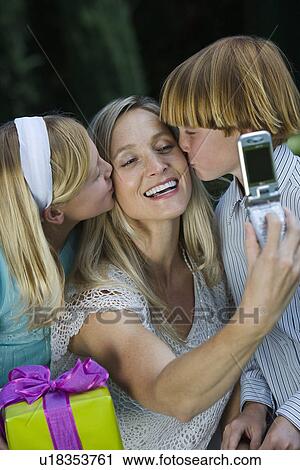 Stock Image - Mid-adult woman taking photograph with mobile phone of her with two children. Fotosearch